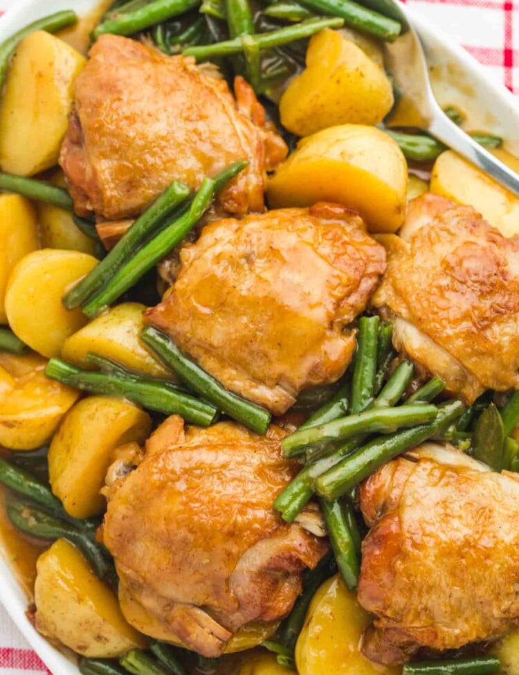 Glazed honey garlic chicken thighs served on a white platter with baby potatoes and green beans, overhead shot.