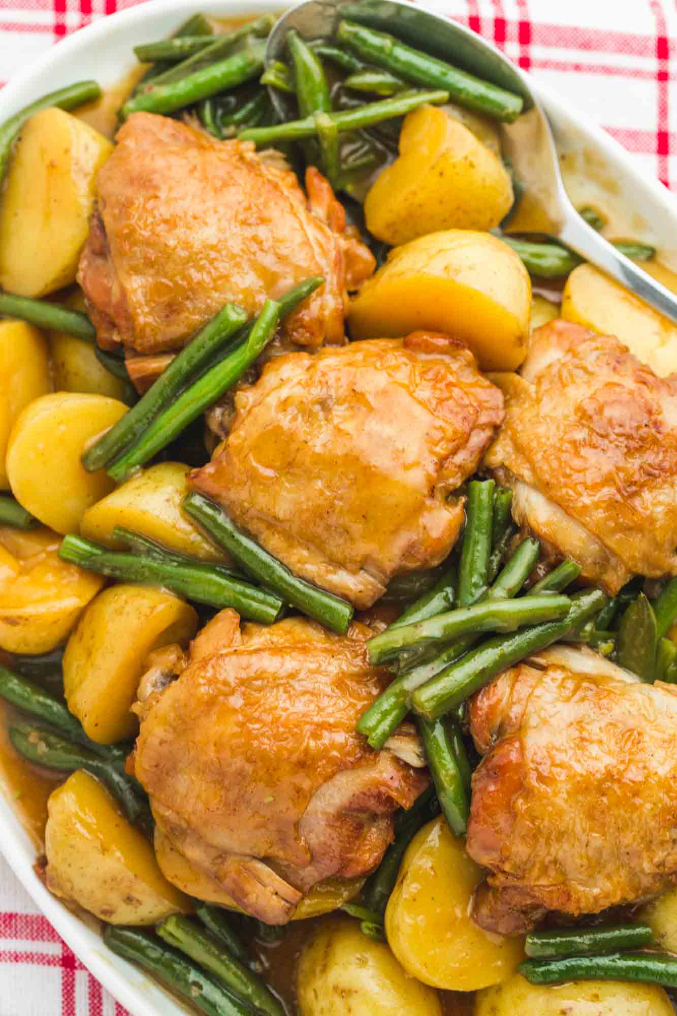 Glazed honey garlic chicken thighs served on a white platter with baby potatoes and green beans, overhead shot.