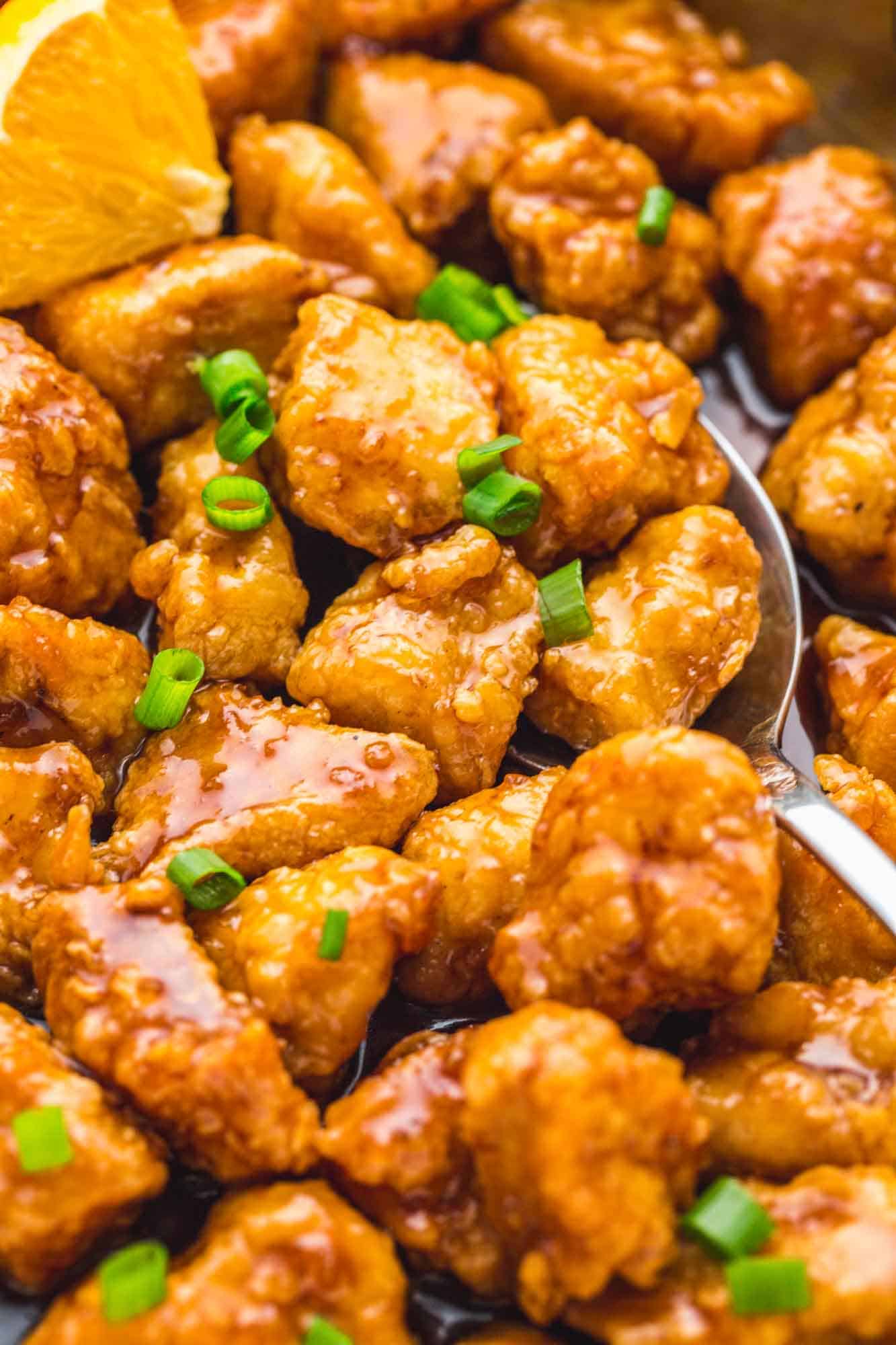 Close up shot of orange chicken in a skillet with a serving spoon