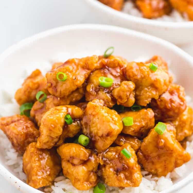 Orange chicken served over a bed of rice in a white speckled bowl