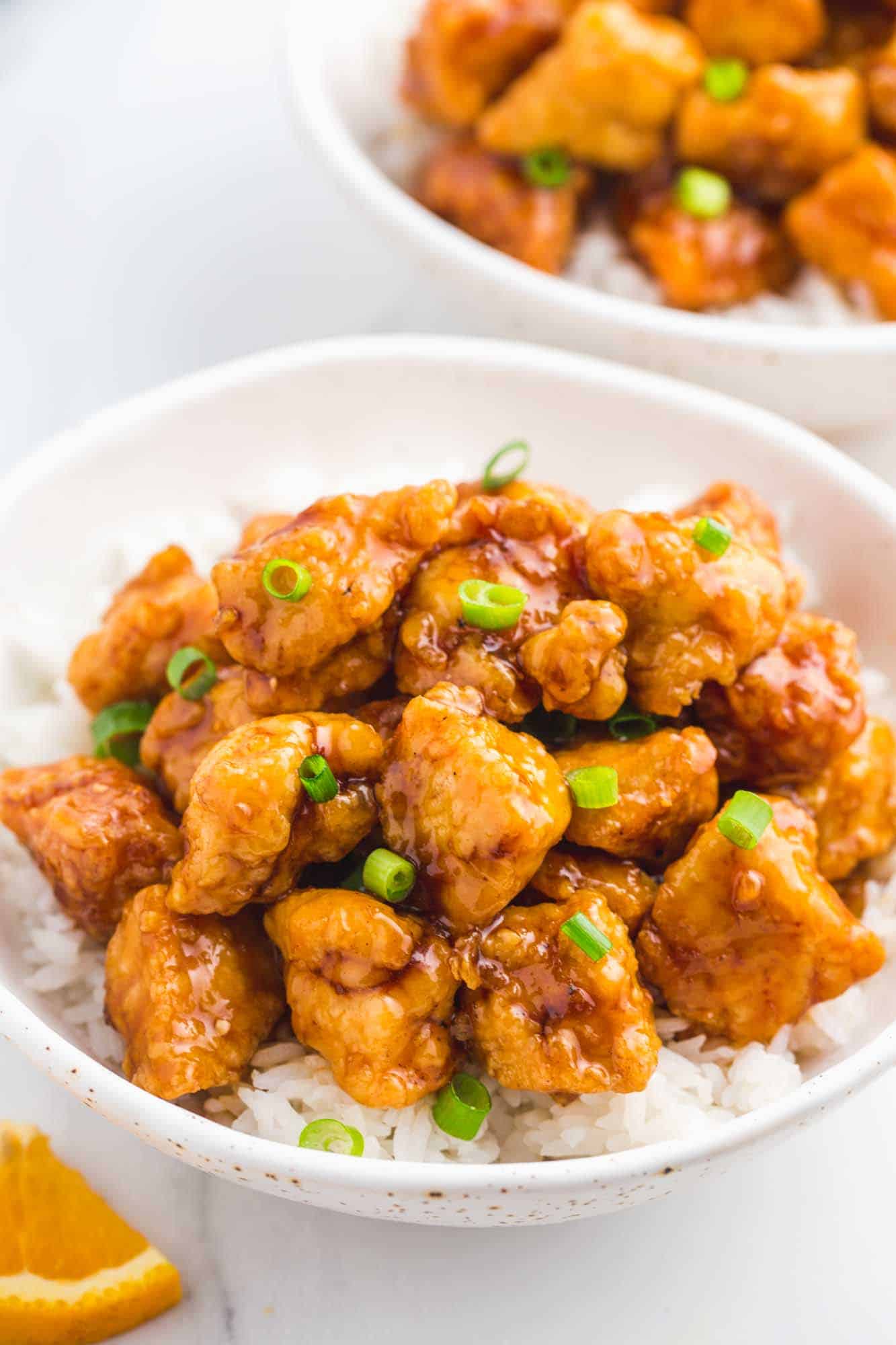 Orange chicken served over a bed of rice in a white speckled bowl