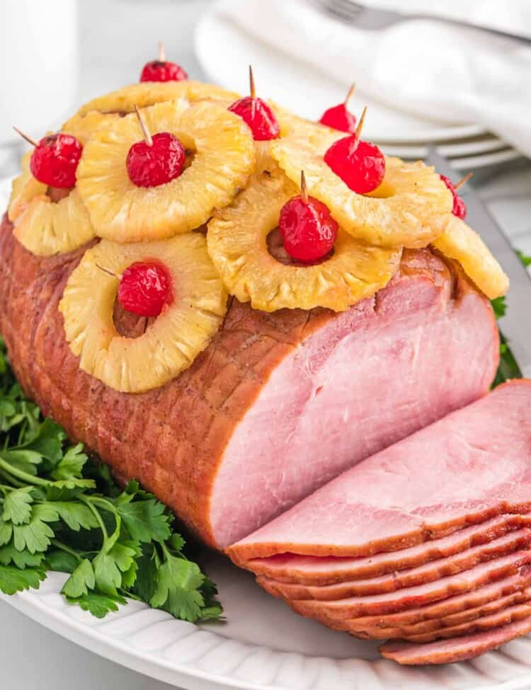 Pineapple ham, sliced, served on a white platter.