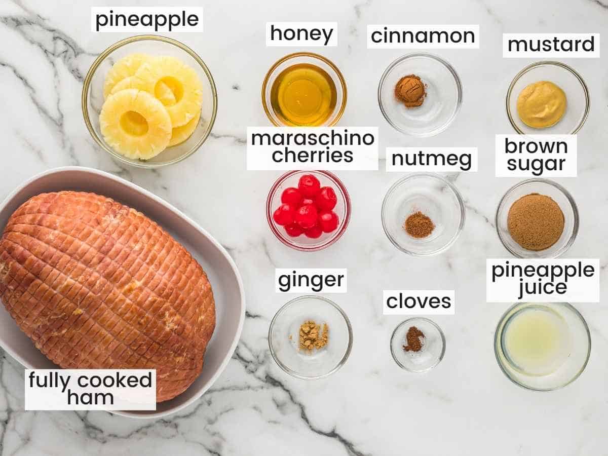 Ingredients needed to make ham with pineapple glaze including fully cooked ham, pineapple, cherries, and seasonings.