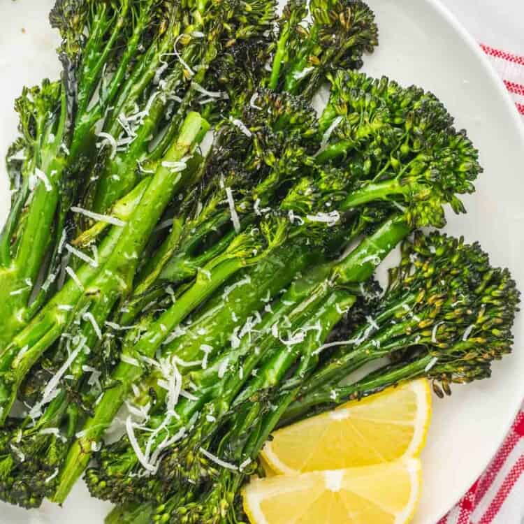 Roasted Broccolini on a plate with lemon slices and grated parmesan.