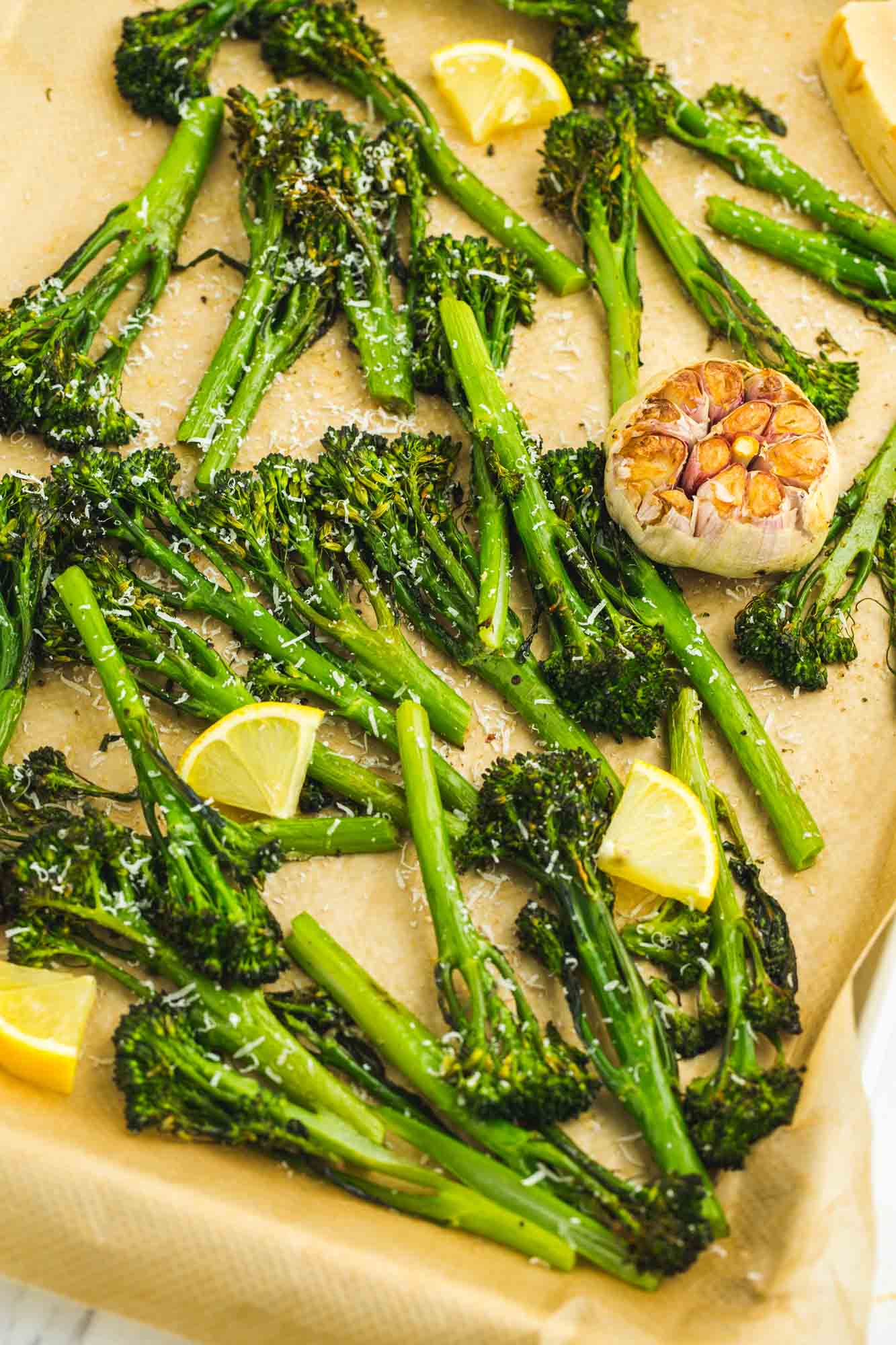 Roasted broccolini and roasted garlic bulb on a sheet pan with lemon slices