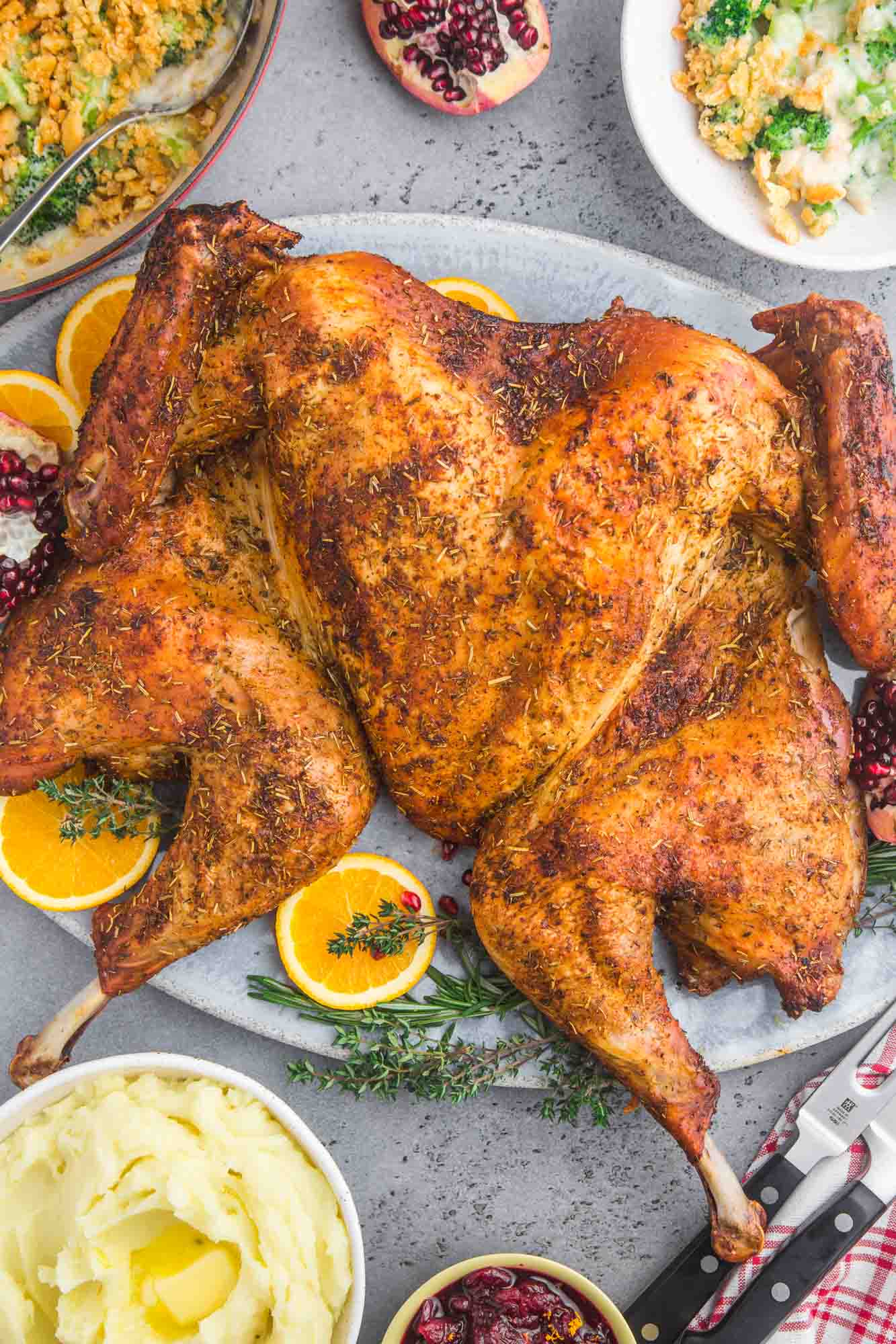 Spatchcocked roasted turkey on a large platter, with sides like mashed potatoes, cranberry sauce, and broccoli casserole.