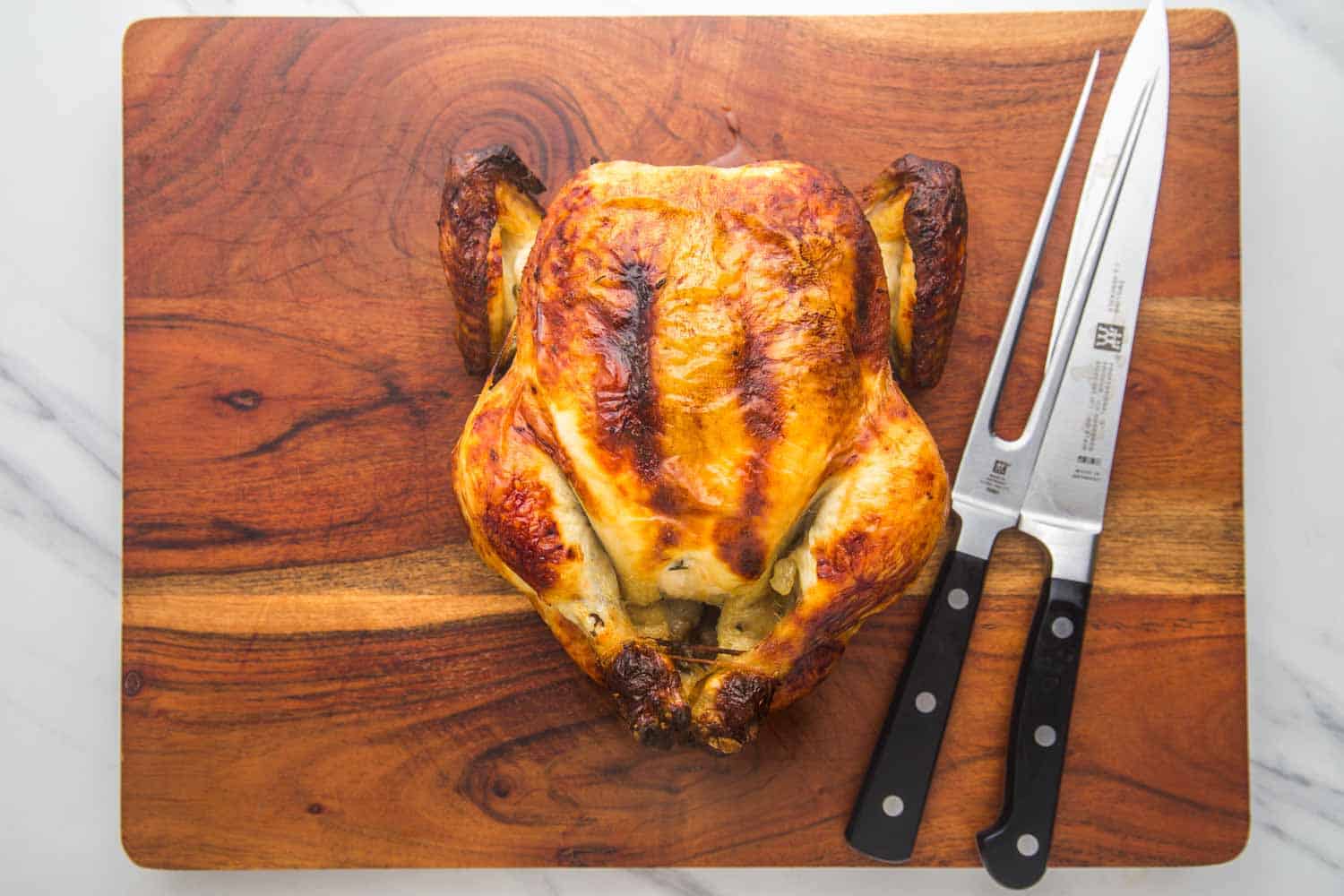 Roast chicken on a wooden cutting board with a sharp carving knife and a carving fork.
