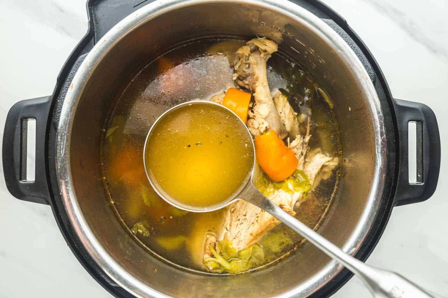 Turkey stock in the instant pot and a ladle with clear stock