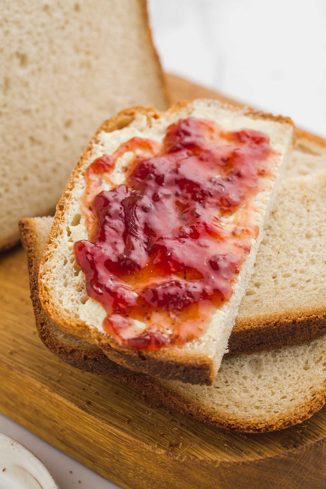 A slice of bread machine white bread with softened butter and strawberry jam