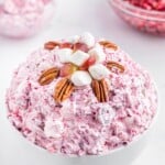 Cranberry fluff salad in a white bowl, topped with pecan halves and marshmallows