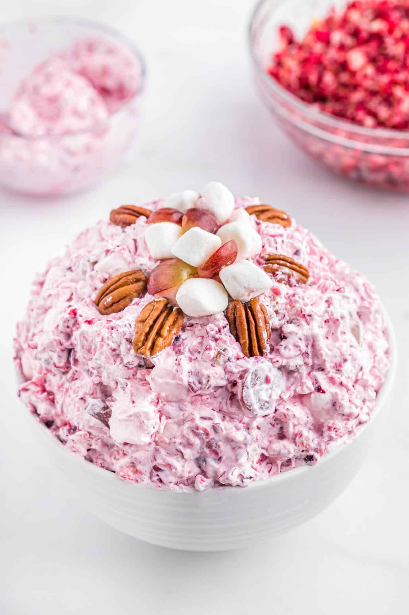 Cranberry fluff salad in a white bowl, topped with pecan halves and marshmallows