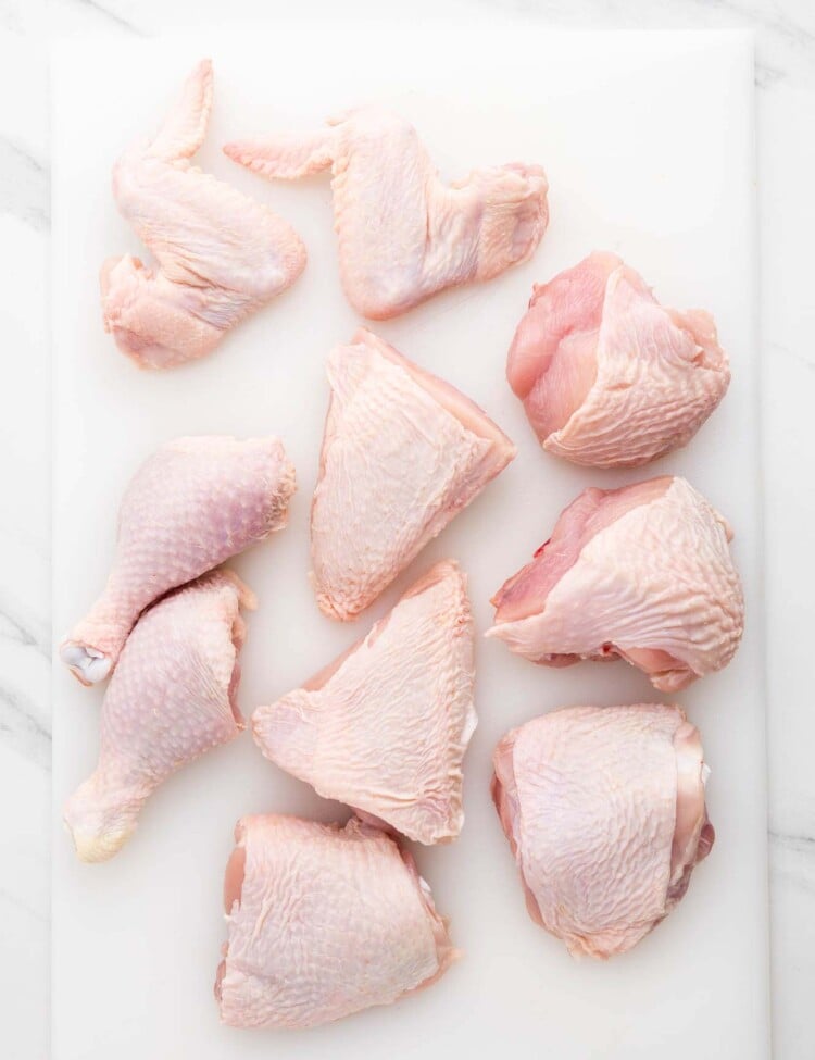 A whole chicken cut up in 10 pieces, placed on a white cutting board
