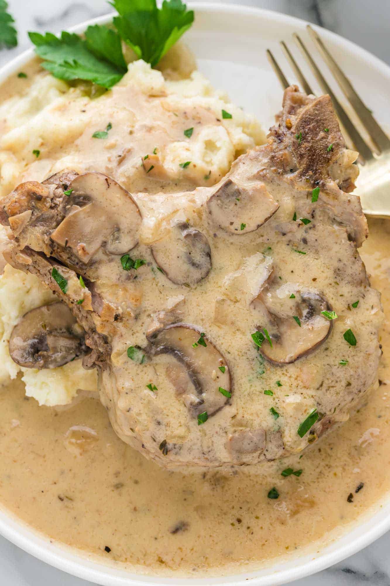 Pork chops with mushroom creamy gravy served over mashed potatoes on a white plate