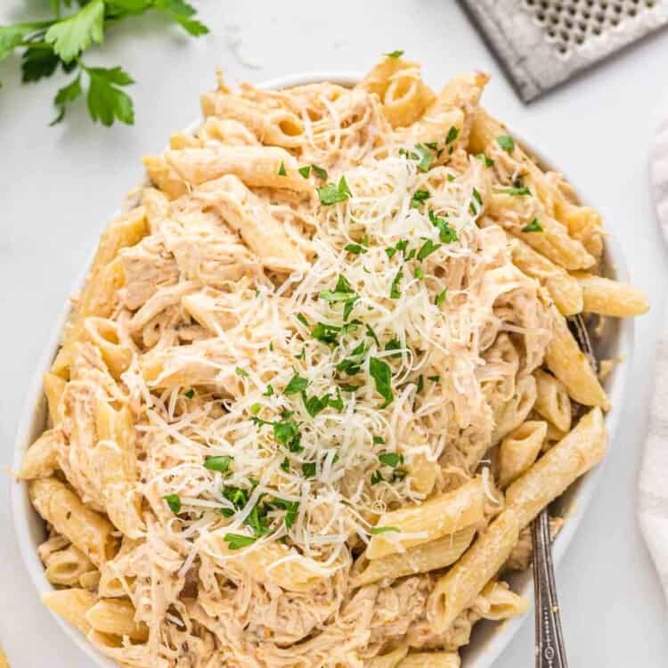 Overhead shot of Olive Garden chicken pasta in a large serving platter, topped with grated parmesan cheese and parsley.