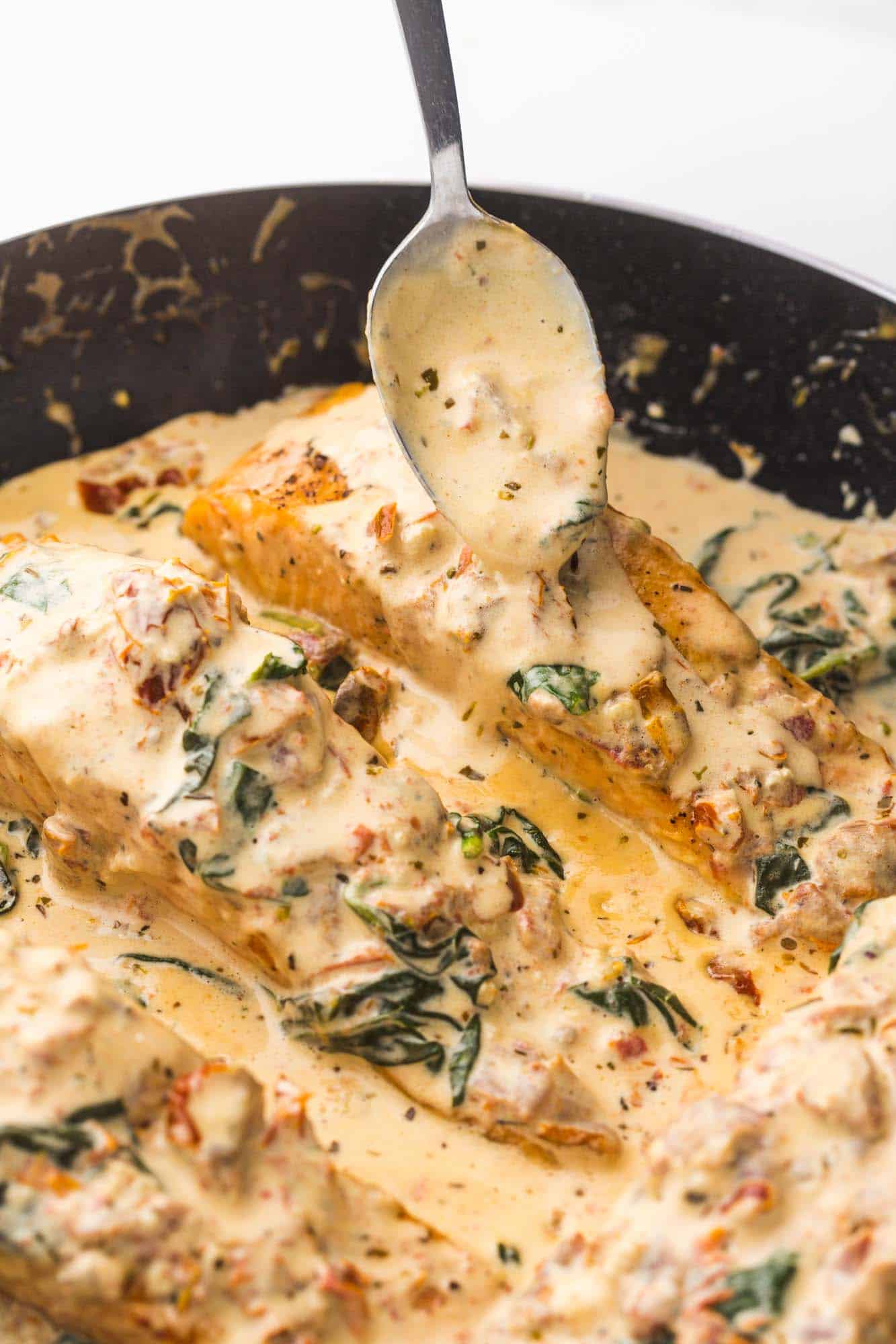 Spooning cream sauce over salmon in the skillet