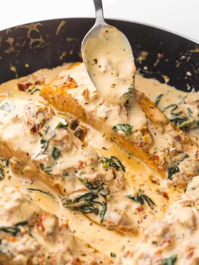 Spooning cream sauce over salmon in the skillet