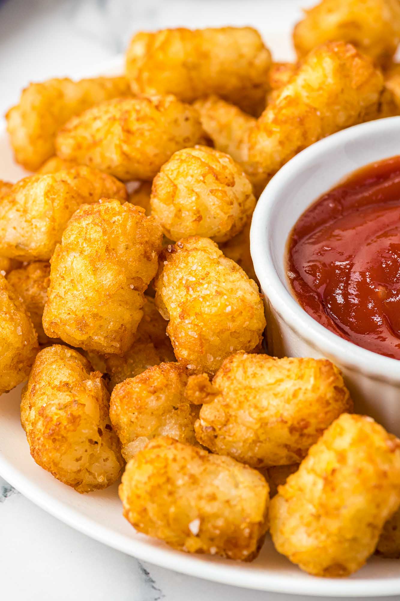 Crispy tater tots served on a plate with a side of ketchup.