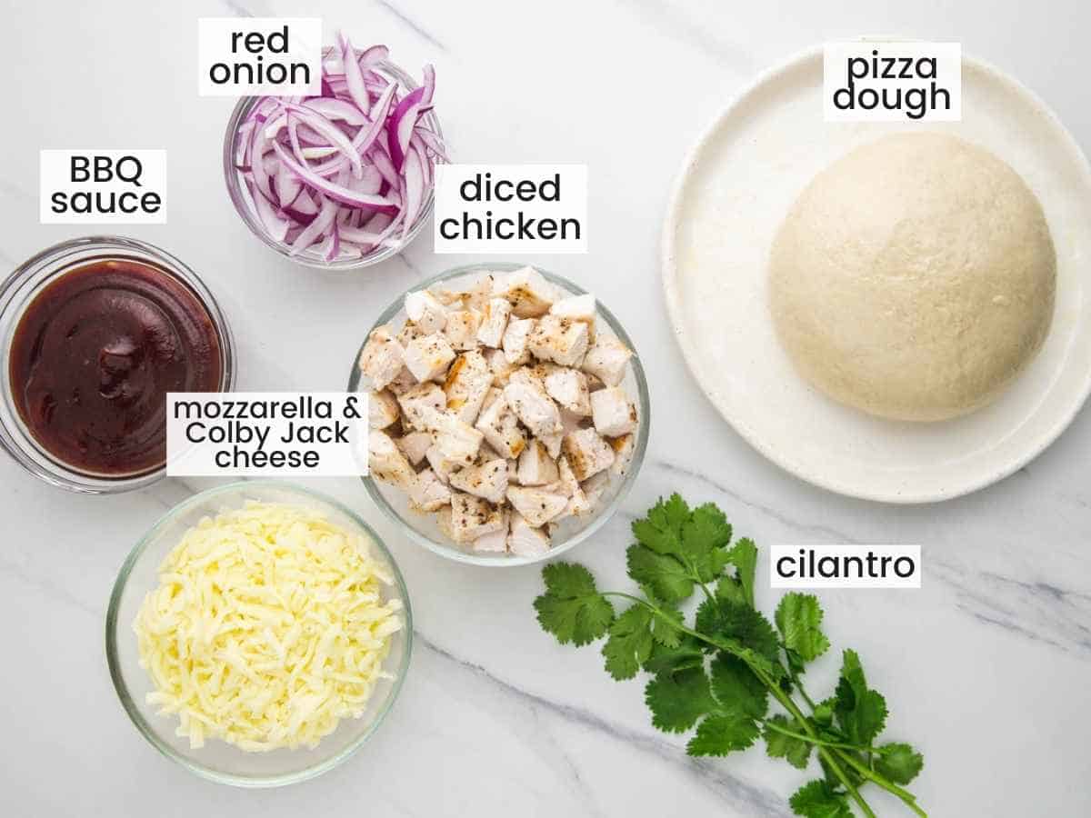 Ingredients needed to make BBQ chicken pizza including pizza dough, red onion, BBQ sauce, cheese, chicken cubes, cilantro.