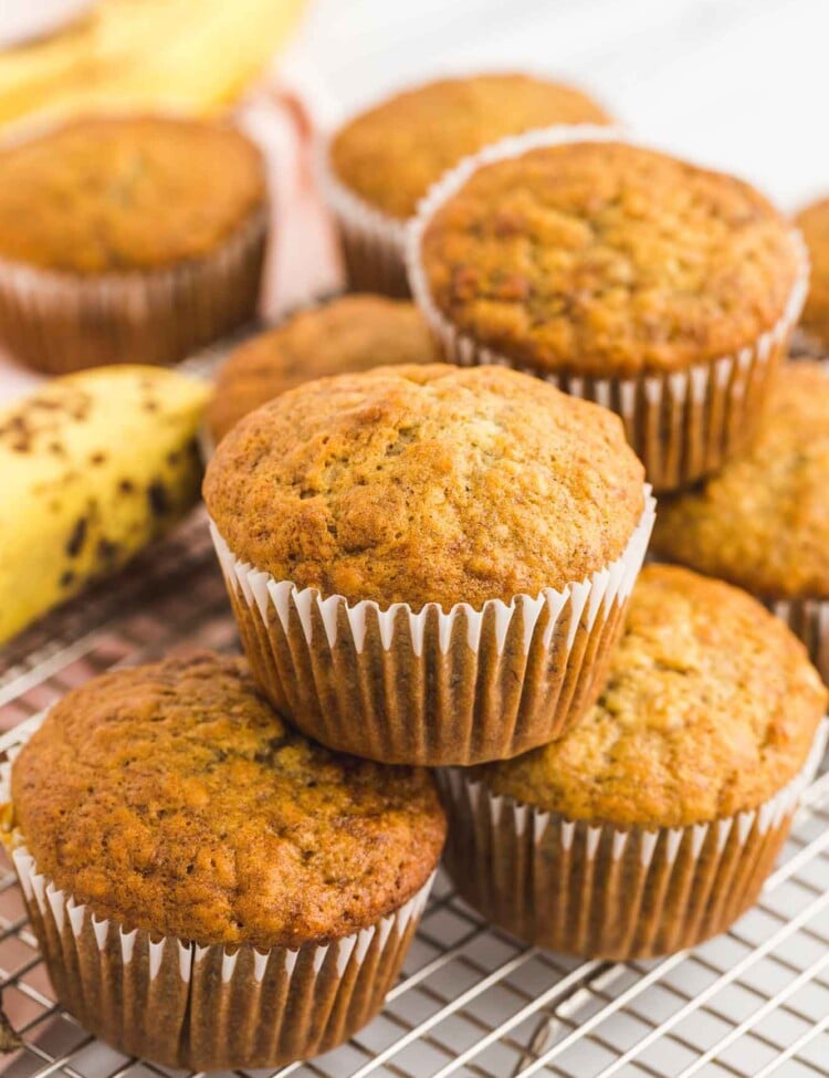 Stacked banana muffins placed on a wire rack, with ripe bananas in the background.