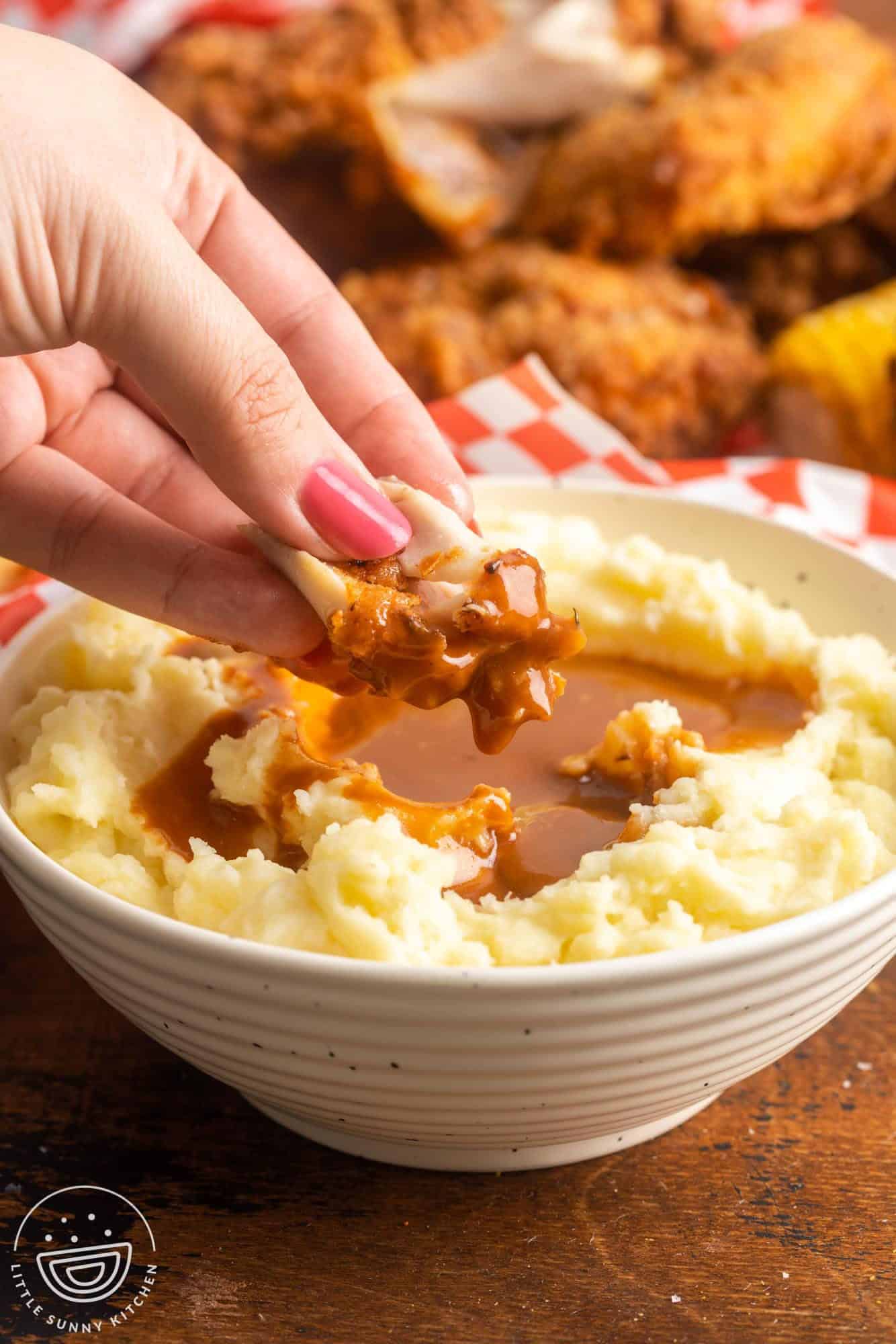 Dipping a piece of fried chicken in mashed potatoes and gravy