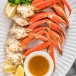 Overhead shot of crab legs served on a large oval white platter with butter dipping sauce and lemon wedges.