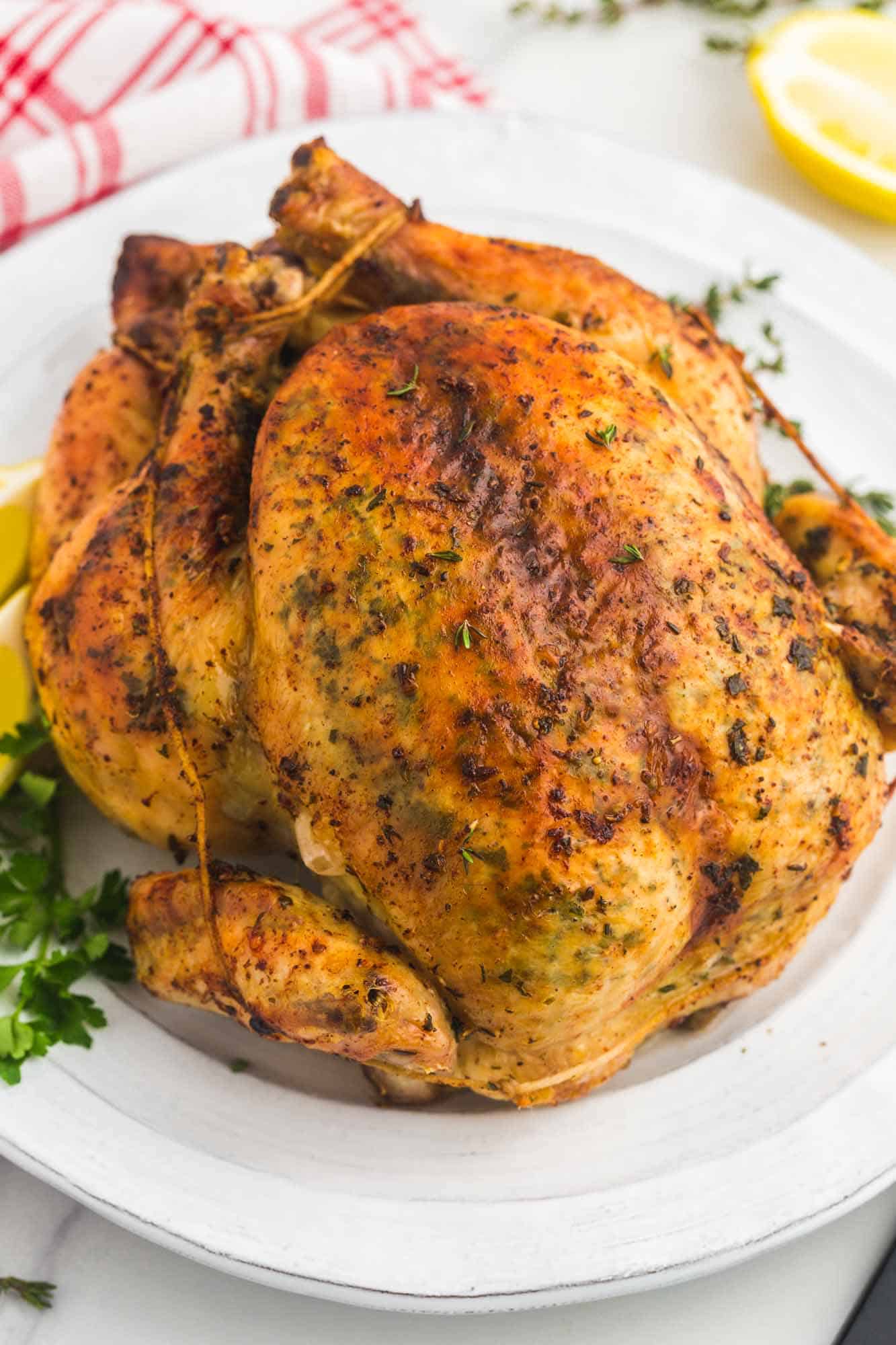 Garlic butter herb roast chicken served on a round platter, with lemon and parsley on the side.