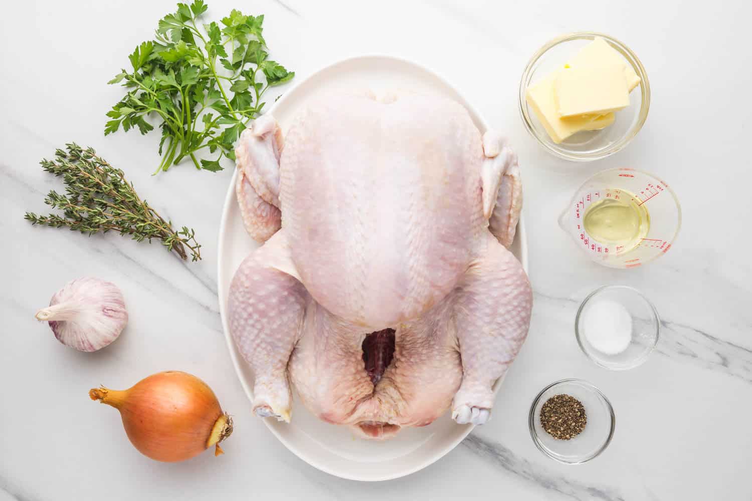 Ingredients needed to make a garlic herb butter roast chicken including one large raw chicken, onion, garlic, butter, salt, pepper, thyme, parsley, and olive oil.
