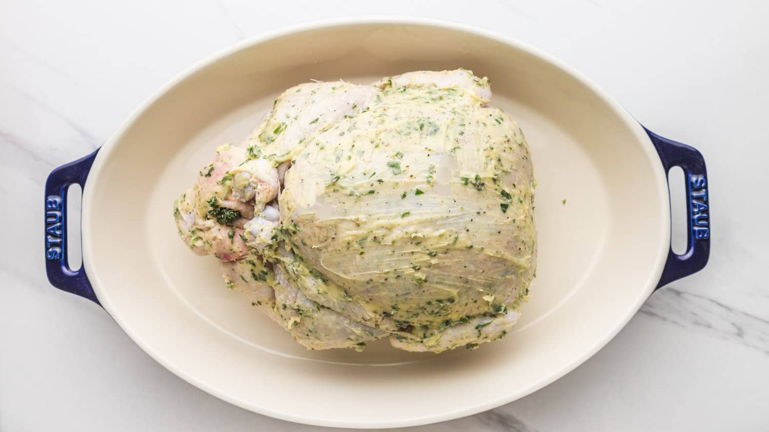 Raw whole chicken slathered with herb butter and placed in an oval roasting ceramic dish by Staub