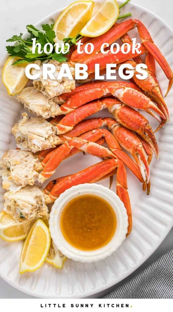 Overhead shot of crab legs served on a large oval white platter with butter dipping sauce and lemon wedges. With overlay text that says "how to cook crab legs"