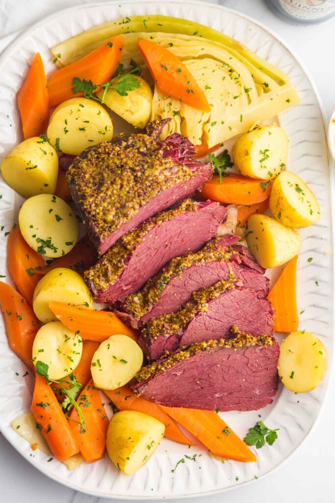 Overhead shot of sliced corned beef brisket served on a white platter with baby potatoes, carrots, and cabbage.