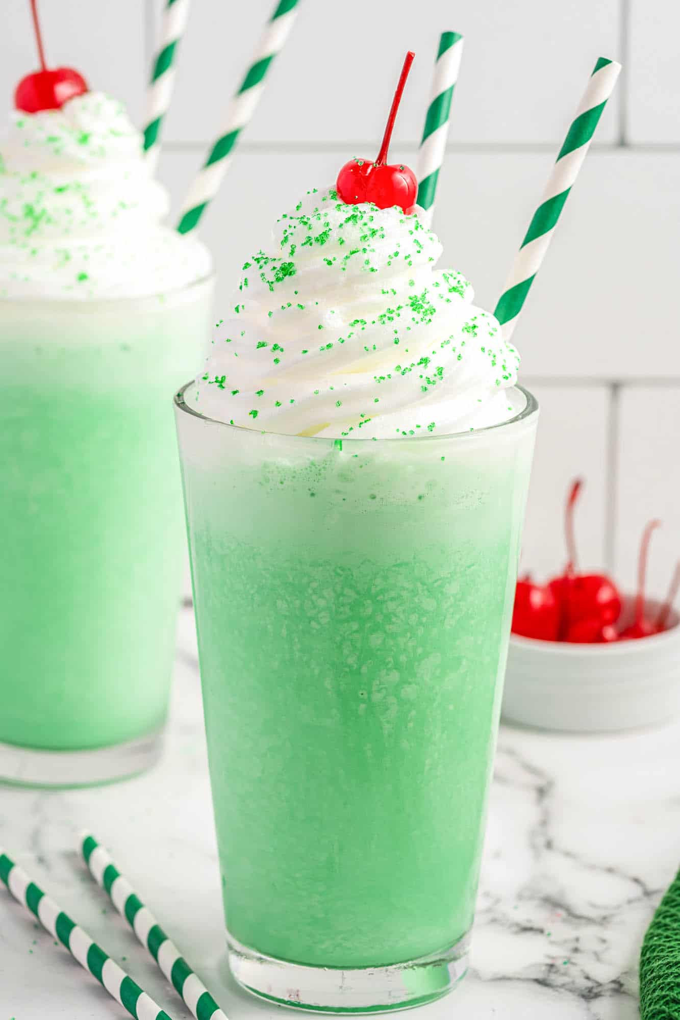 Milkshake glasses filled with green shamrock shake, topped with whipped cream and maraschino cherries.