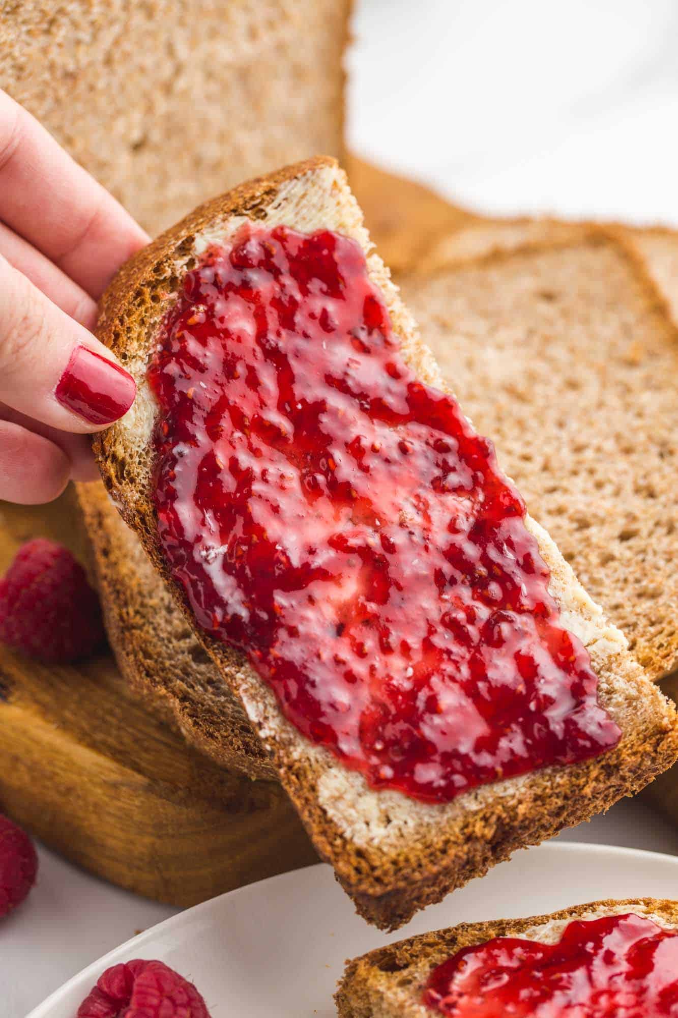 Holding a piece of whole wheat bread with raspberry jam on it