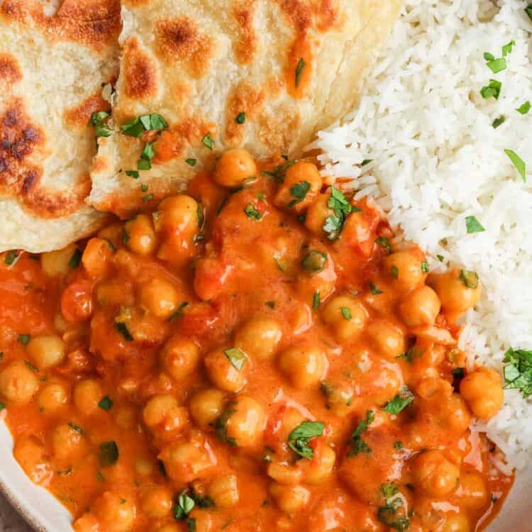 Creamy coconut chickpea curry served in a bowl with white rice, naan, and fresh cilantro.