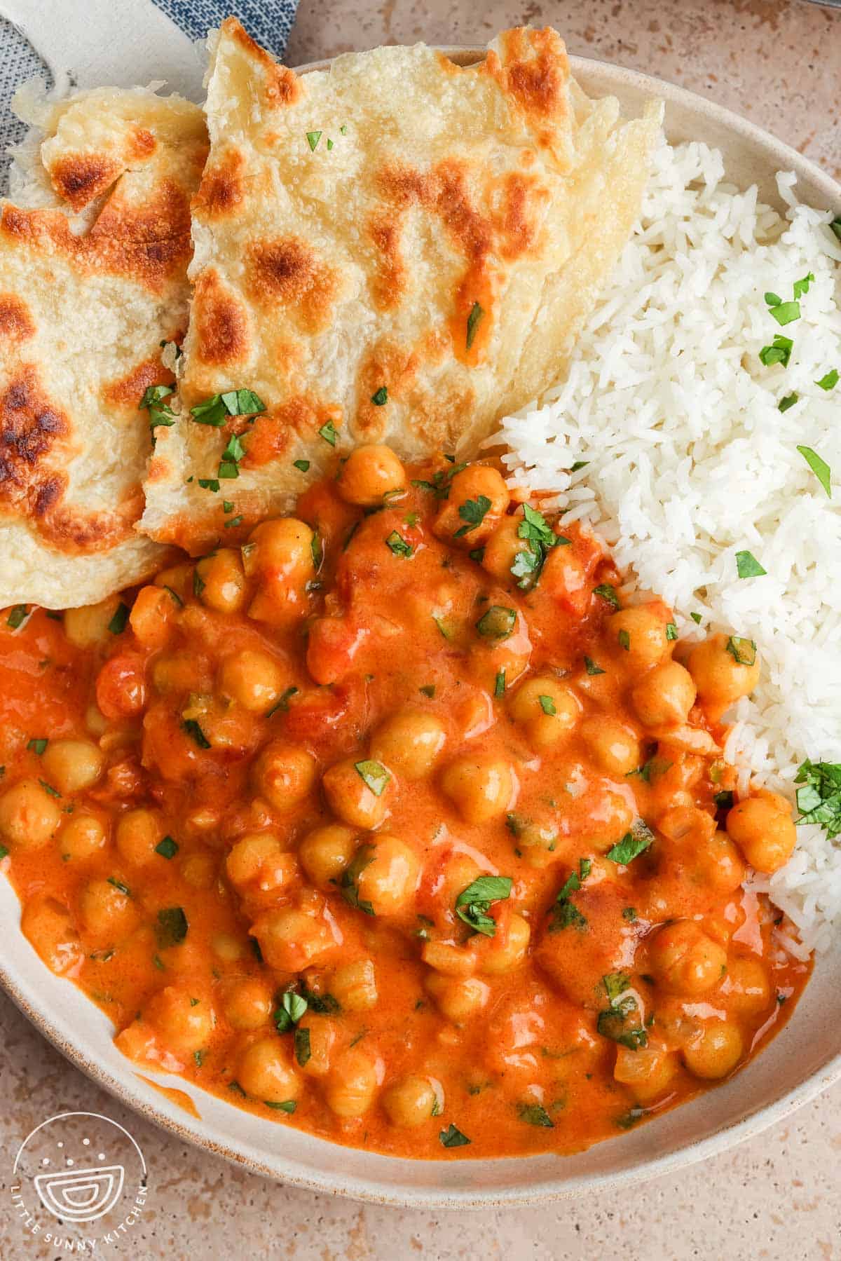 Creamy coconut chickpea curry served in a bowl with white rice, naan, and fresh cilantro.