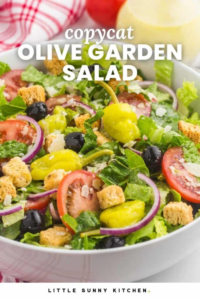 Copycat Olive Garden salad with lettuce, tomatoes, pepperoncini, black olives, red onion, croutons, and parmesan in a white bowl