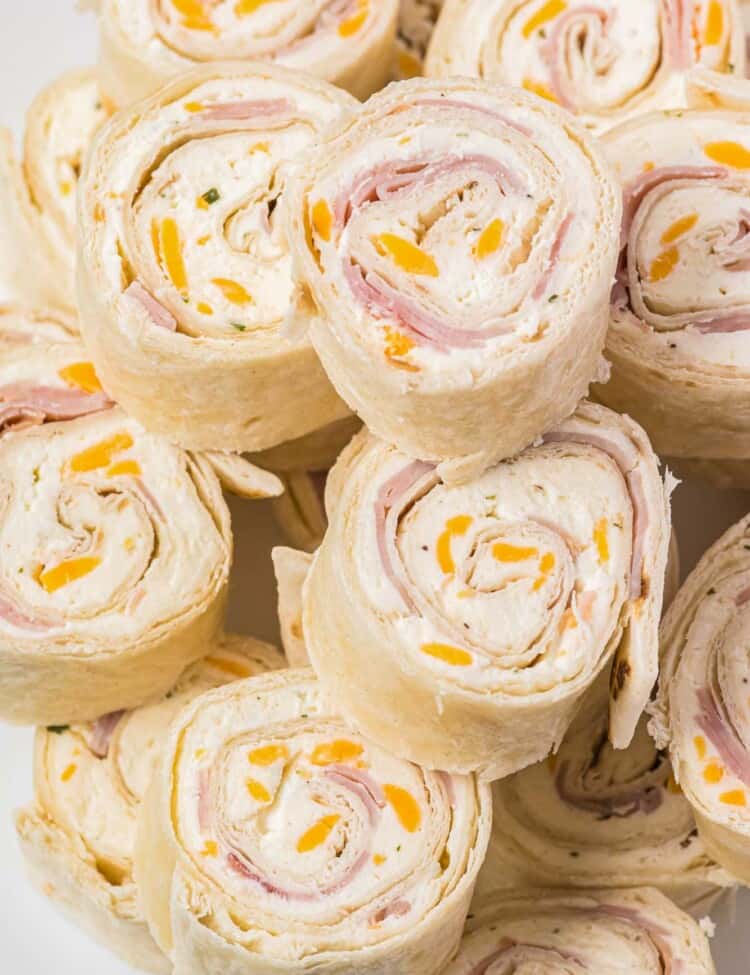 Stacked ham and cheese pinwheels, served on a white plate.