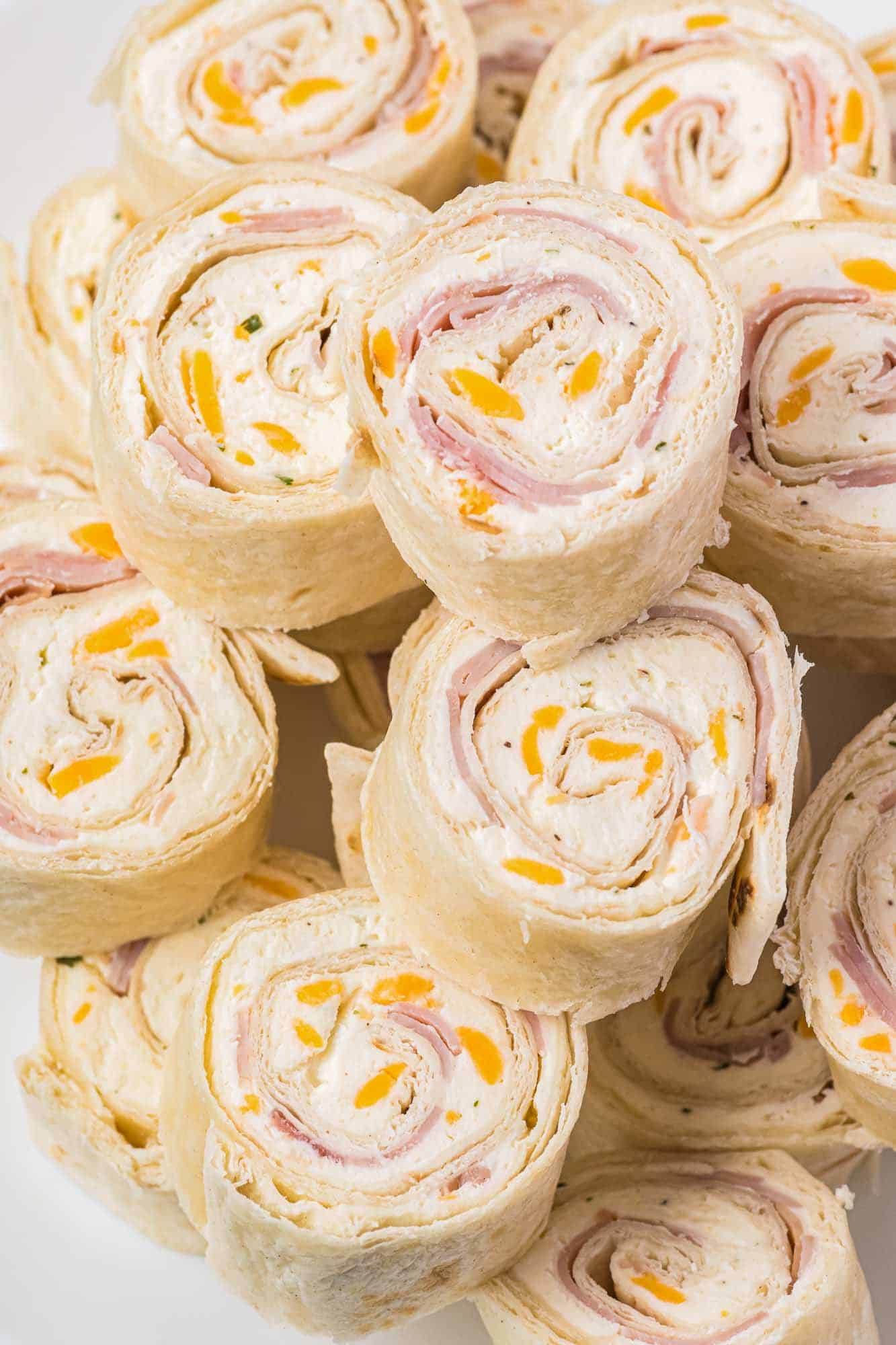 Stacked ham and cheese pinwheels, served on a white plate.