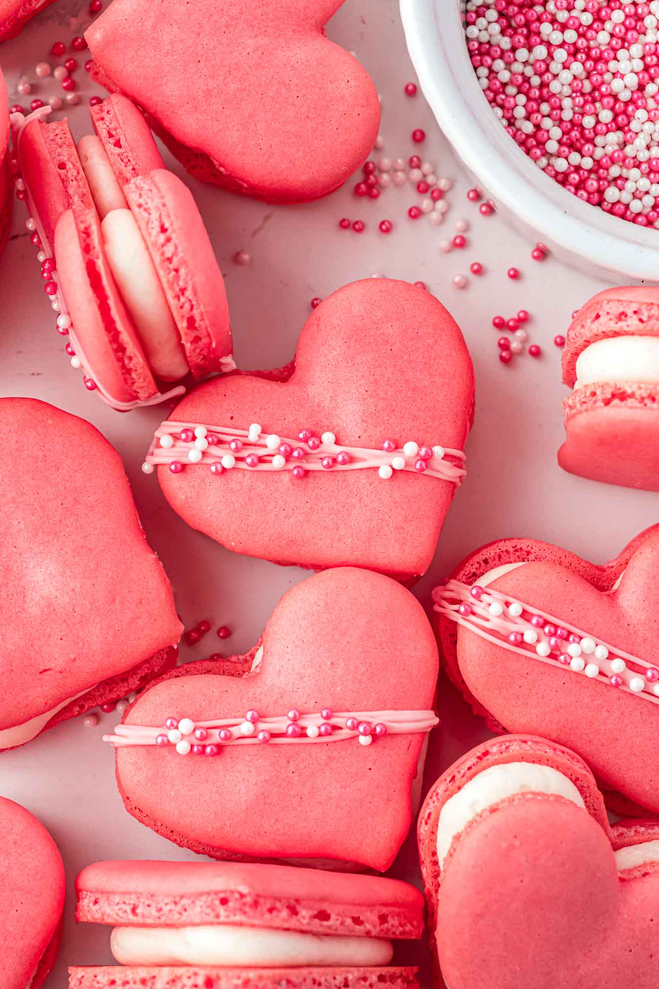Overhead shot of heart shaped pink macarons decorated with sprinkles, filled with vanilla buttercream.
