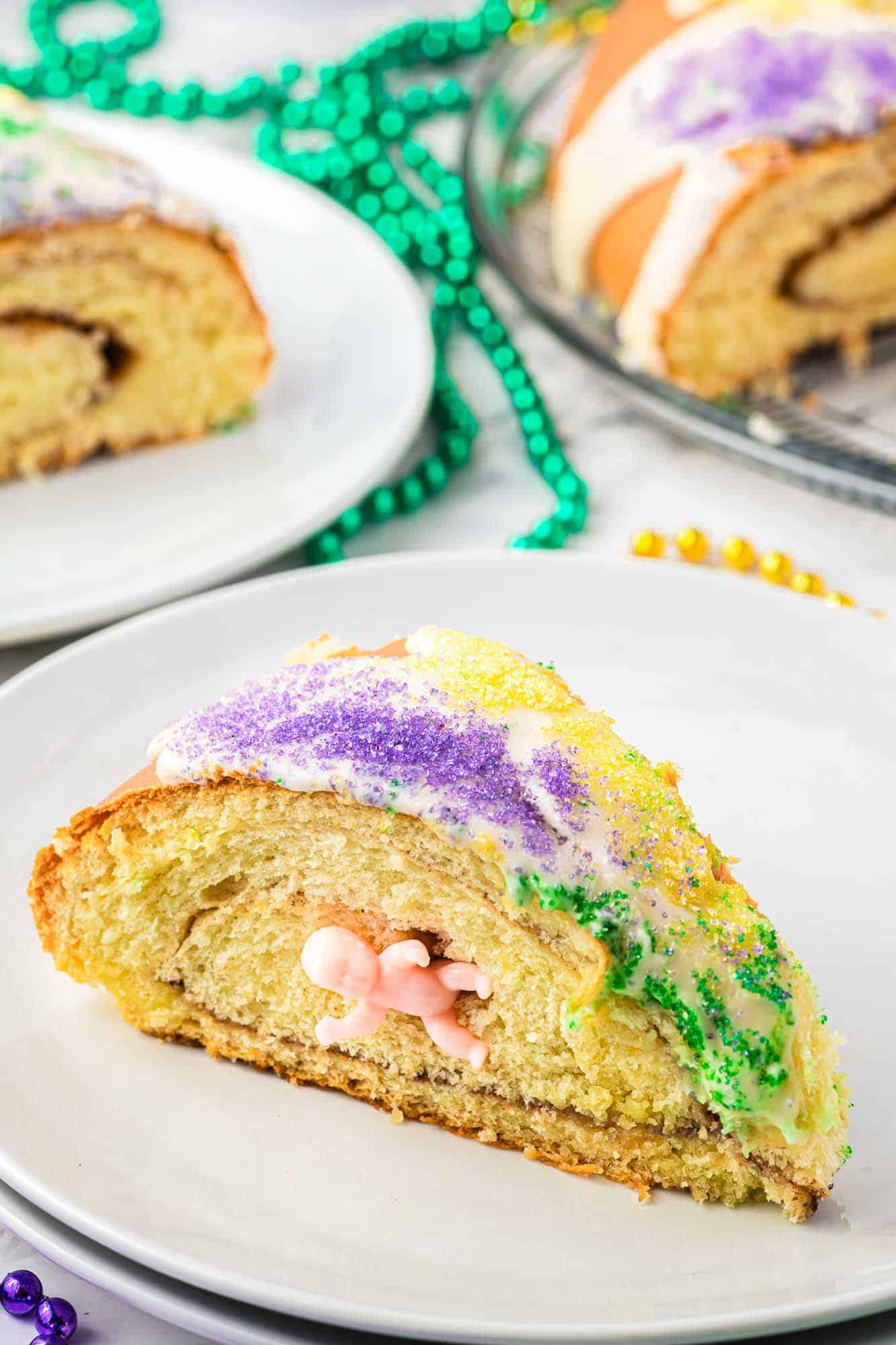 A slice of king cake with a plasic baby inside, served on a white plate.