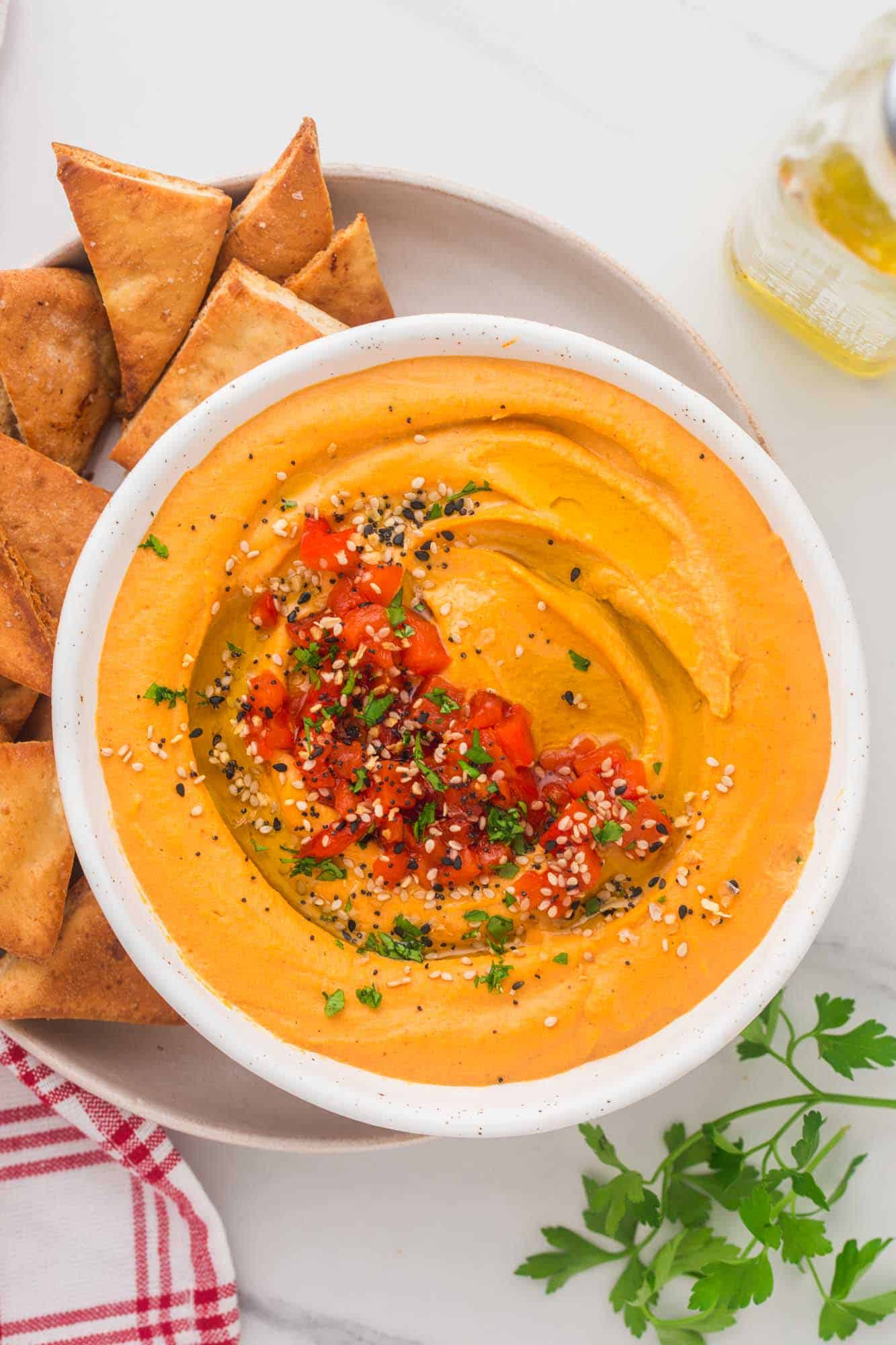 Overhead shot of Roasted Red Pepper Hummus in a white bowl, served with pita chips on the side.