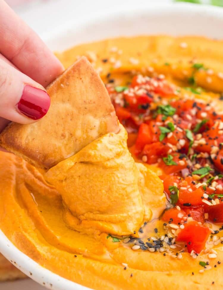 Dipping pita chips in roasted red pepper hummus