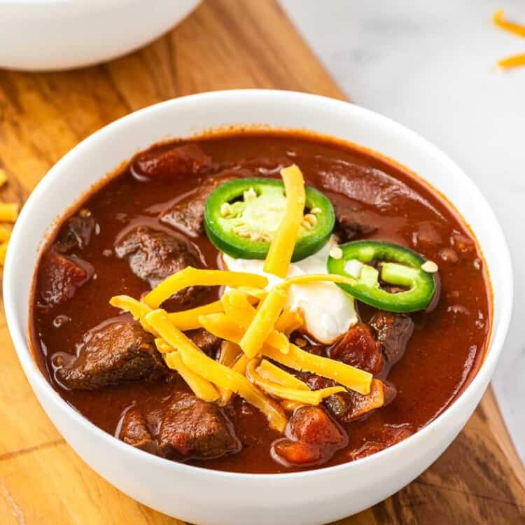 A bowl of texas chili topped with cheese, sour cream, and sliced jalapeno.