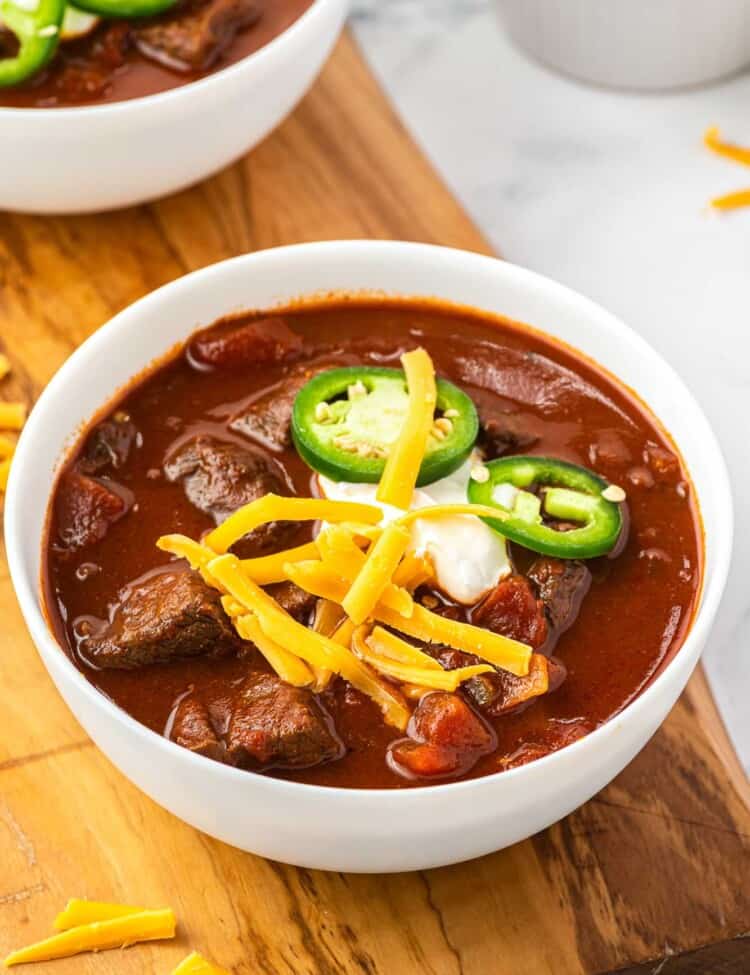 A bowl of texas chili topped with cheese, sour cream, and sliced jalapeno.