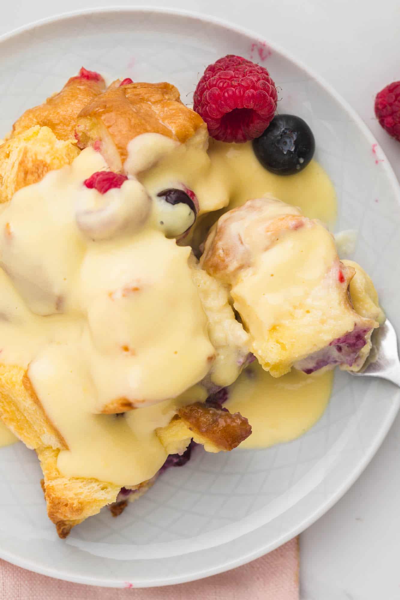 Overhead shot of a serving of bread pudding with berries on a small plate, topped with creamy vanilla sauce.