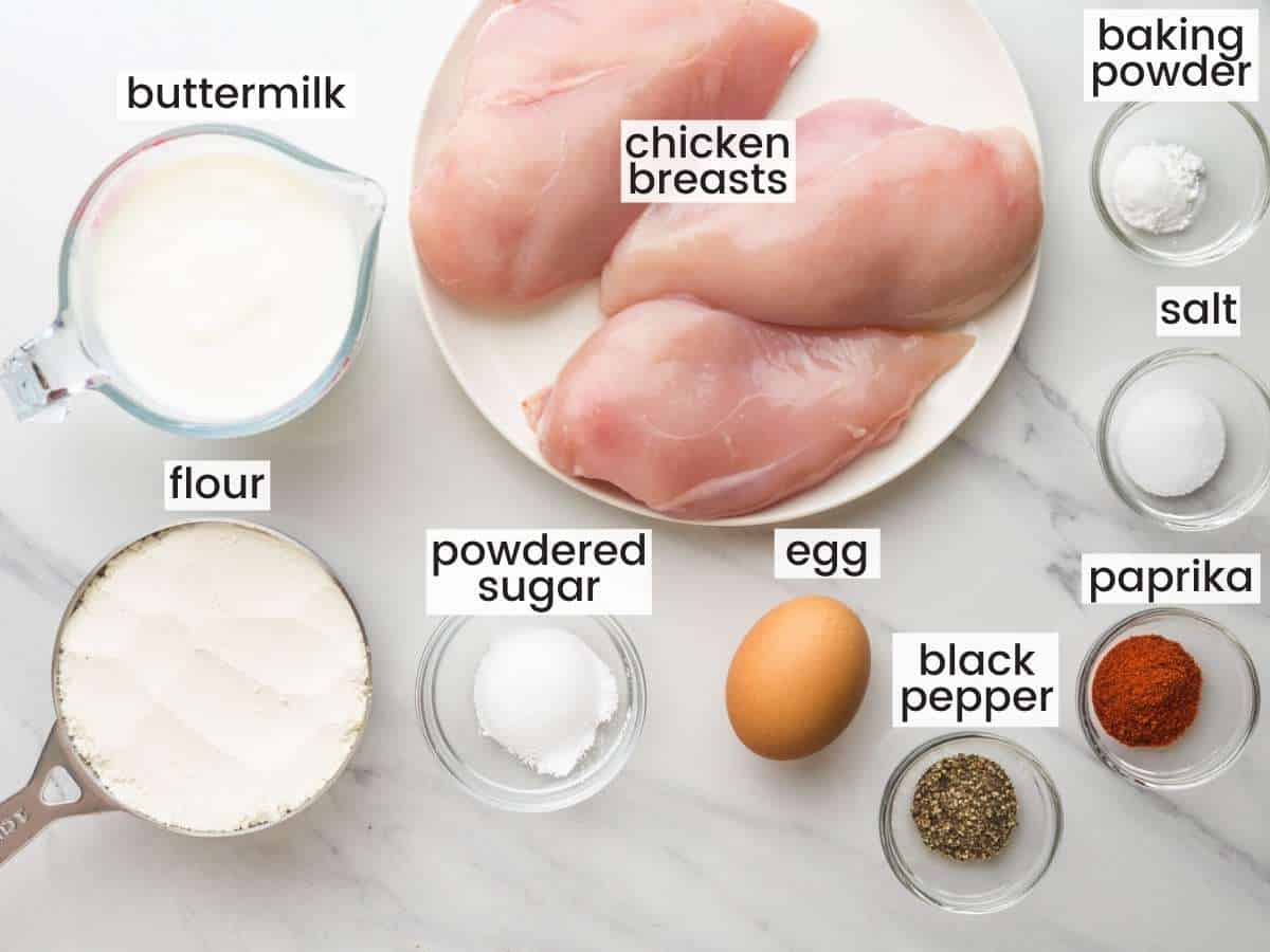 The ingredients for making homemade chick fil a nuggets all measured out into separate bowls, on a marble countertop