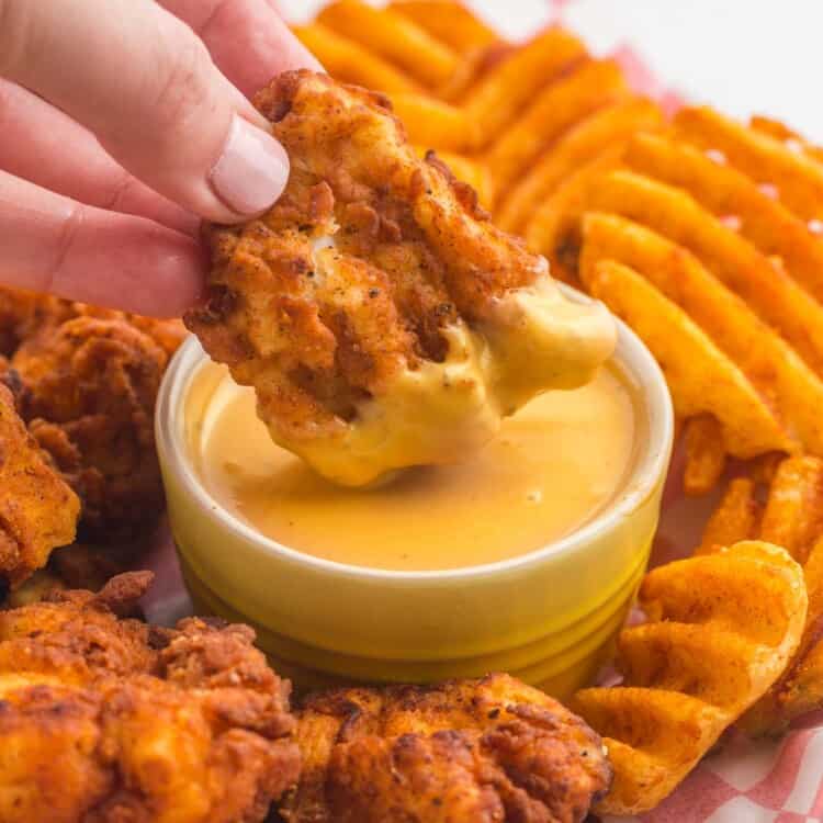 a plate of chicken nuggets and waffle fries with a cup of chick fil a sauce in the middle being used as a dip