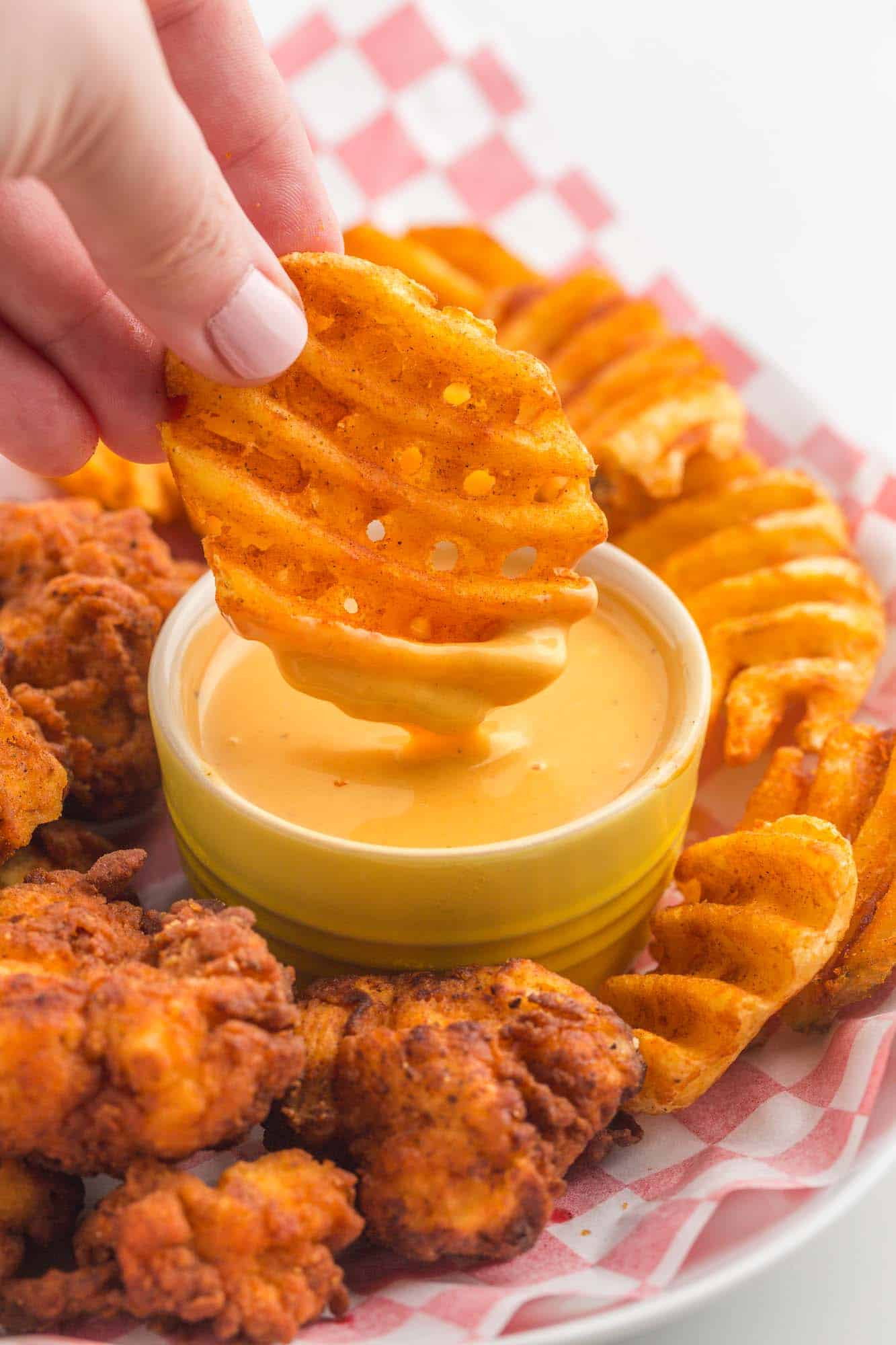 a hand dipping a waffle fry into a cup of chick fil a sauce on a plate of chicken nuggets