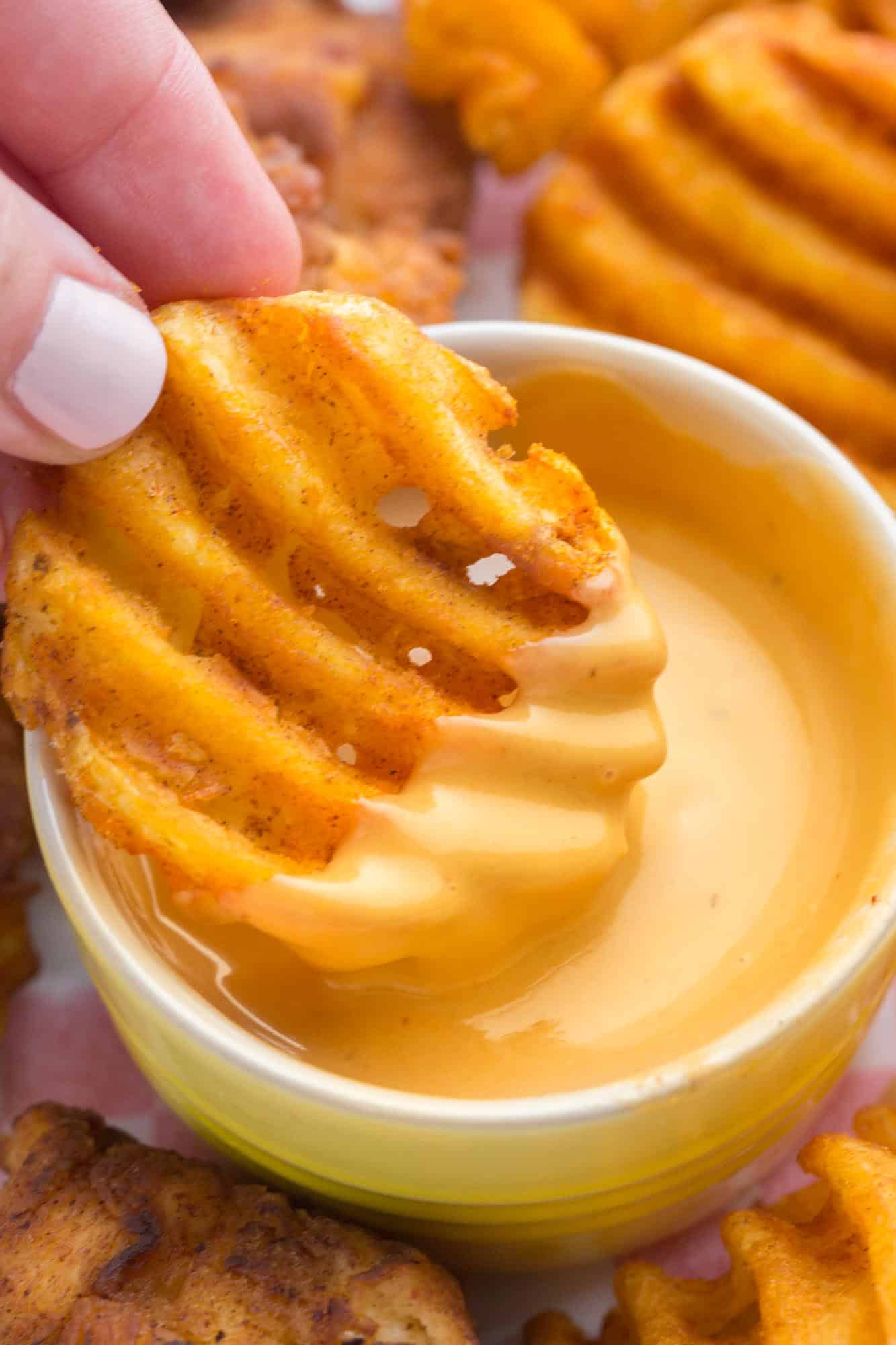 a waffle fry being dipped into a small cup of chick fil a sauce