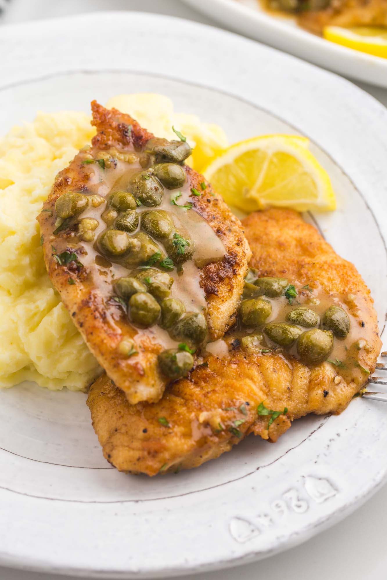 Two chicken piccata cutlets served on mashed potatoes, and caper sauce. Plated.