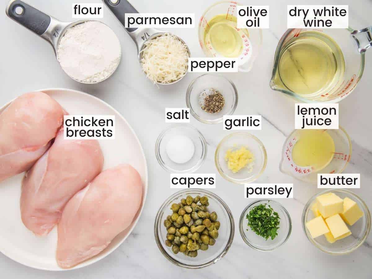 Ingredients needed to make chicken piccata including chicken breasts, flour, parmesan, butter, white wine, garlic, capers, parsley, salt and pepper.